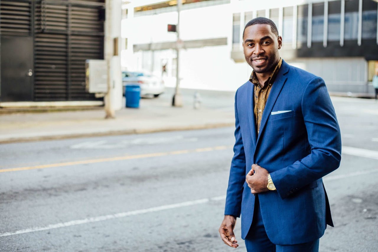 A confident businessman in a blue suit smiling outdoors in an urban setting during the day.